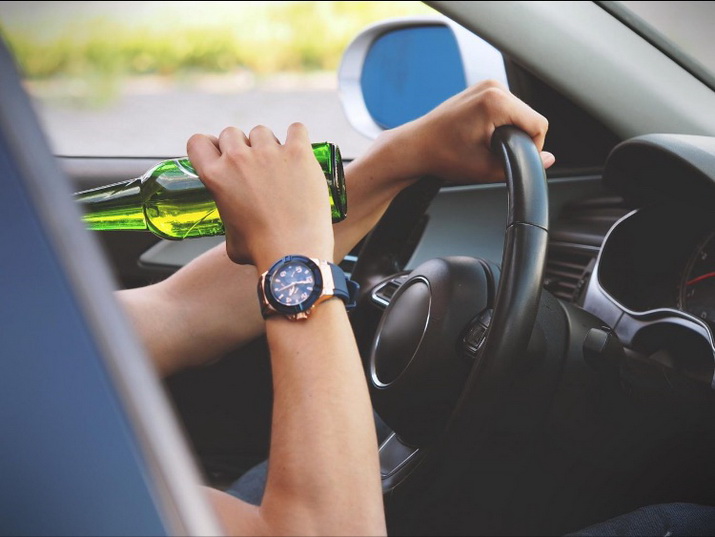 Autofahrer mit Hand am Steuer und Bierflasche in anderer Hand