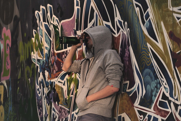 Junger Mann im Hoodie an Graffiti-Wand mit Flasche am Mund