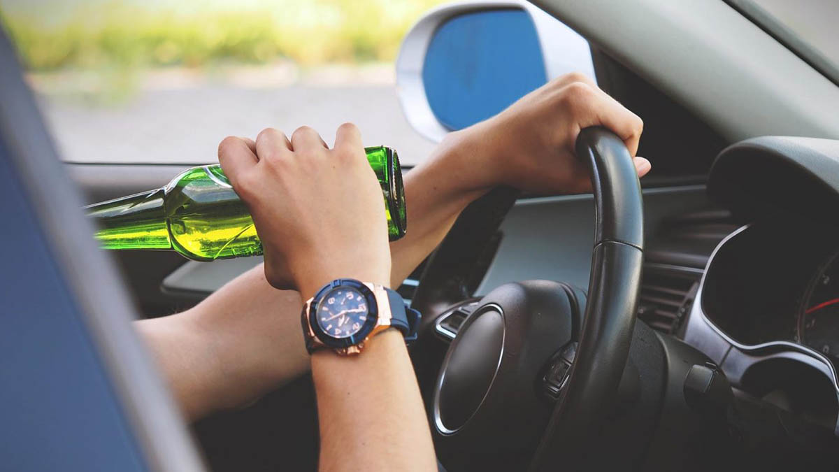 Autofahrerhände am Steuer und mit Bierflasche