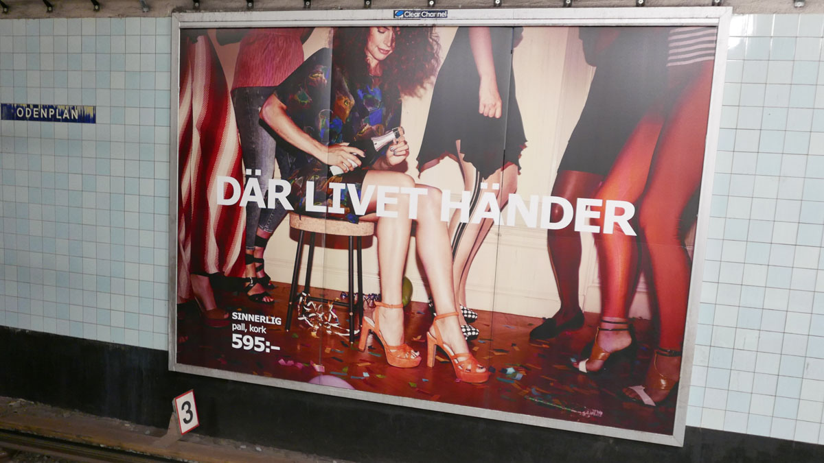 Werbetafel in Stockholmer U-Bahn-Station mit Frau, die sich ein Glas füllt und der Aufschrift "Wo das Leben passiert"