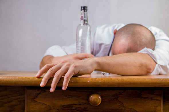 Betrunkener Mann schläft auf Tisch mit leerer Flasche in der Hand