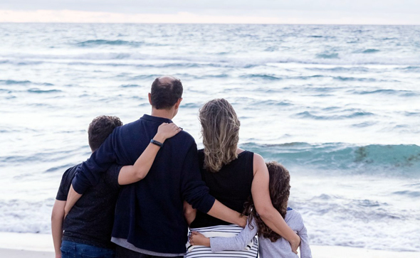 Elternpaar mit zwei Kindern im Arm blickt auf offenes Meer