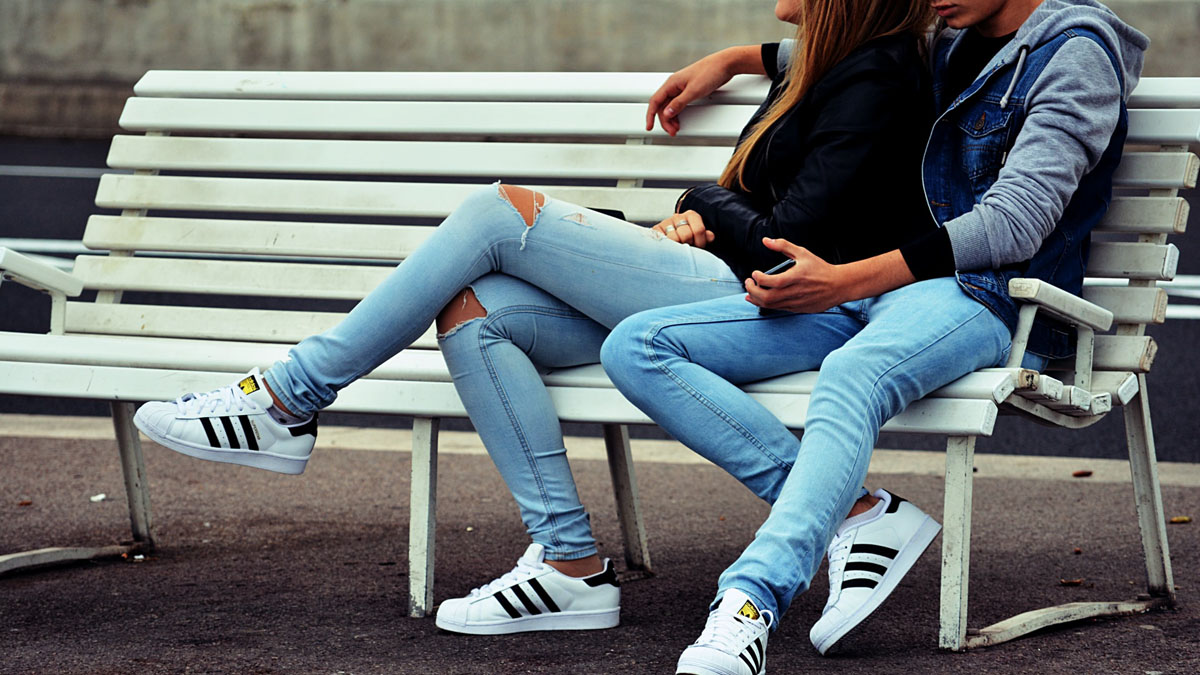 Jugendliches Paar sitzt auf Parkbank mit Smartphone in der Hand