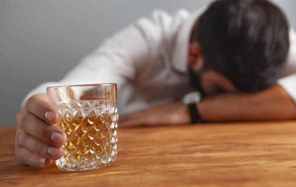 Mann mit Whiskyglas in der Hand schläft auf Tischplatte