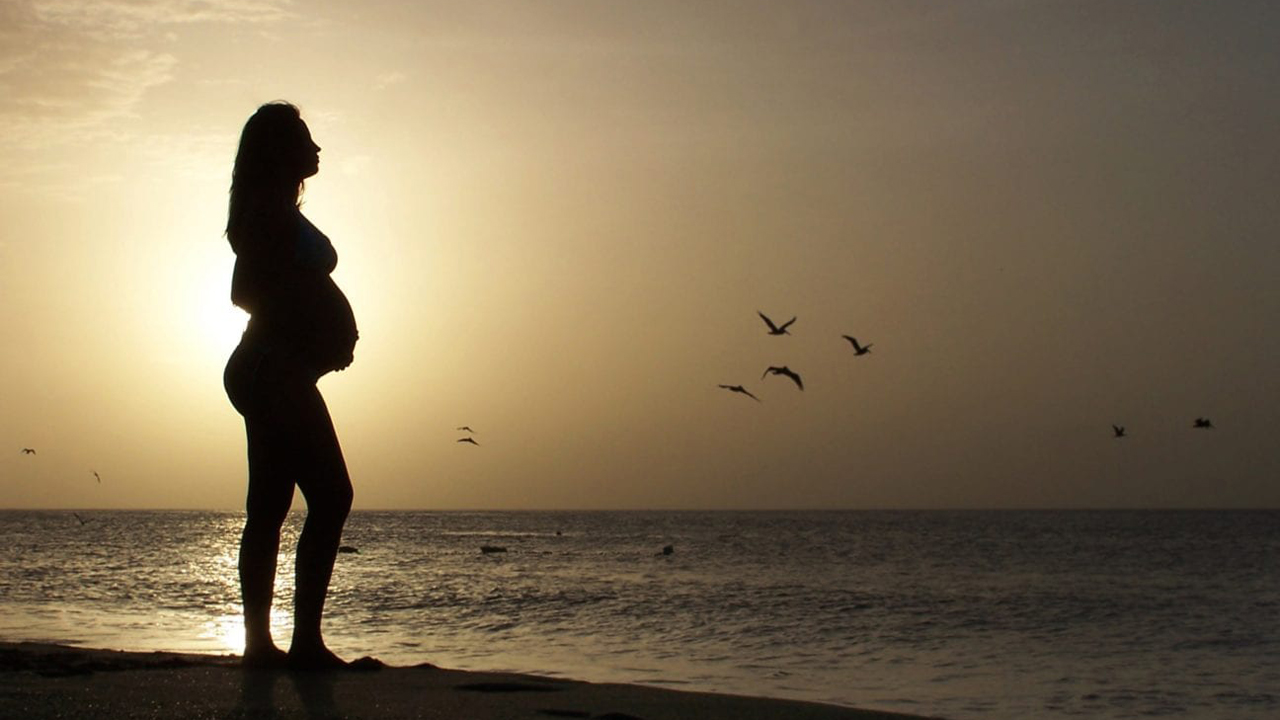 Silhouette einer schwangeren Frau am Strand bei Sonnenuntergang.