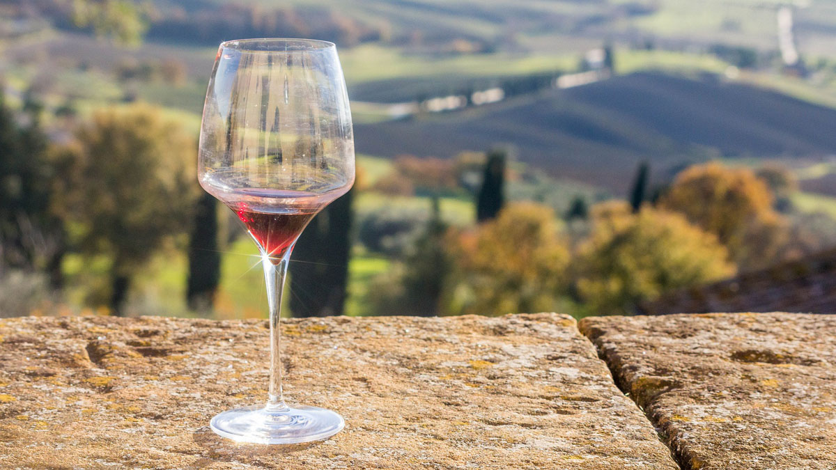 Weinglas auf Mauer vor Blick über Landschaft in der Toskana