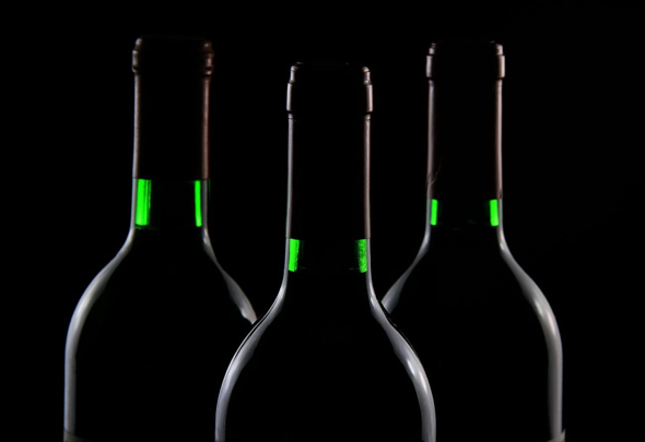 Drei schwarze Weinflaschen vor schwarzem Hintergrund