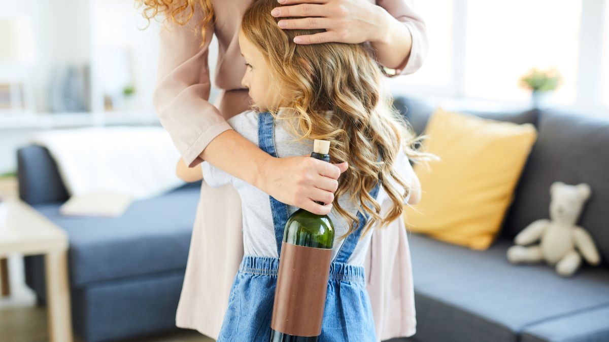 Mutter umarmt Tochter mit Weinflasche in der Hand