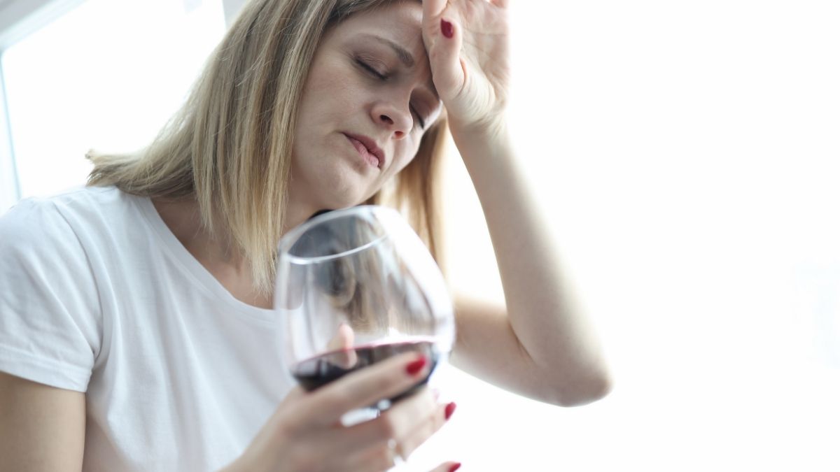 Erschöpfte Frau mit Hand an Stirn hält Weinglas