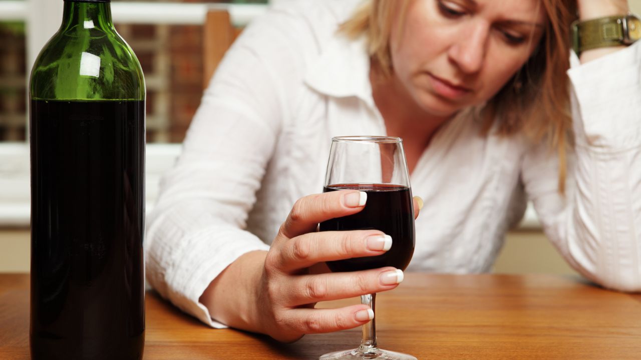 Enttäuschte Frau sitzt mit Wein an einem Tisch.
