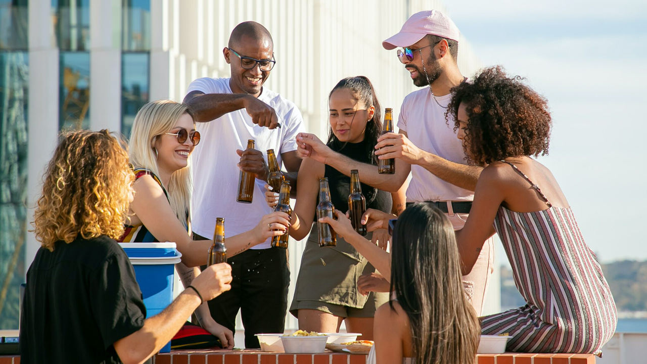 Gruppe junger Menschen im Freien beim Anstoßen mit Bierflaschen.
