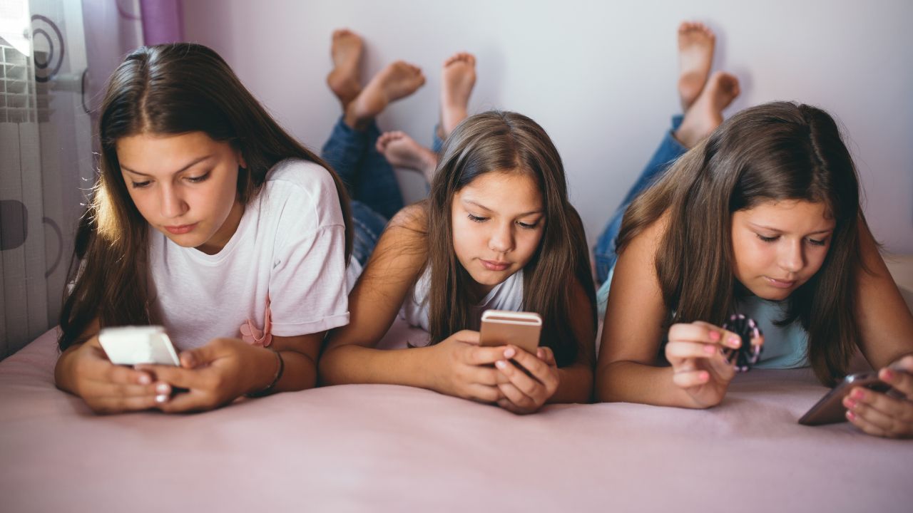 Drei auf dem Bauch liegende Jugendliche nutzen soziale Medien.