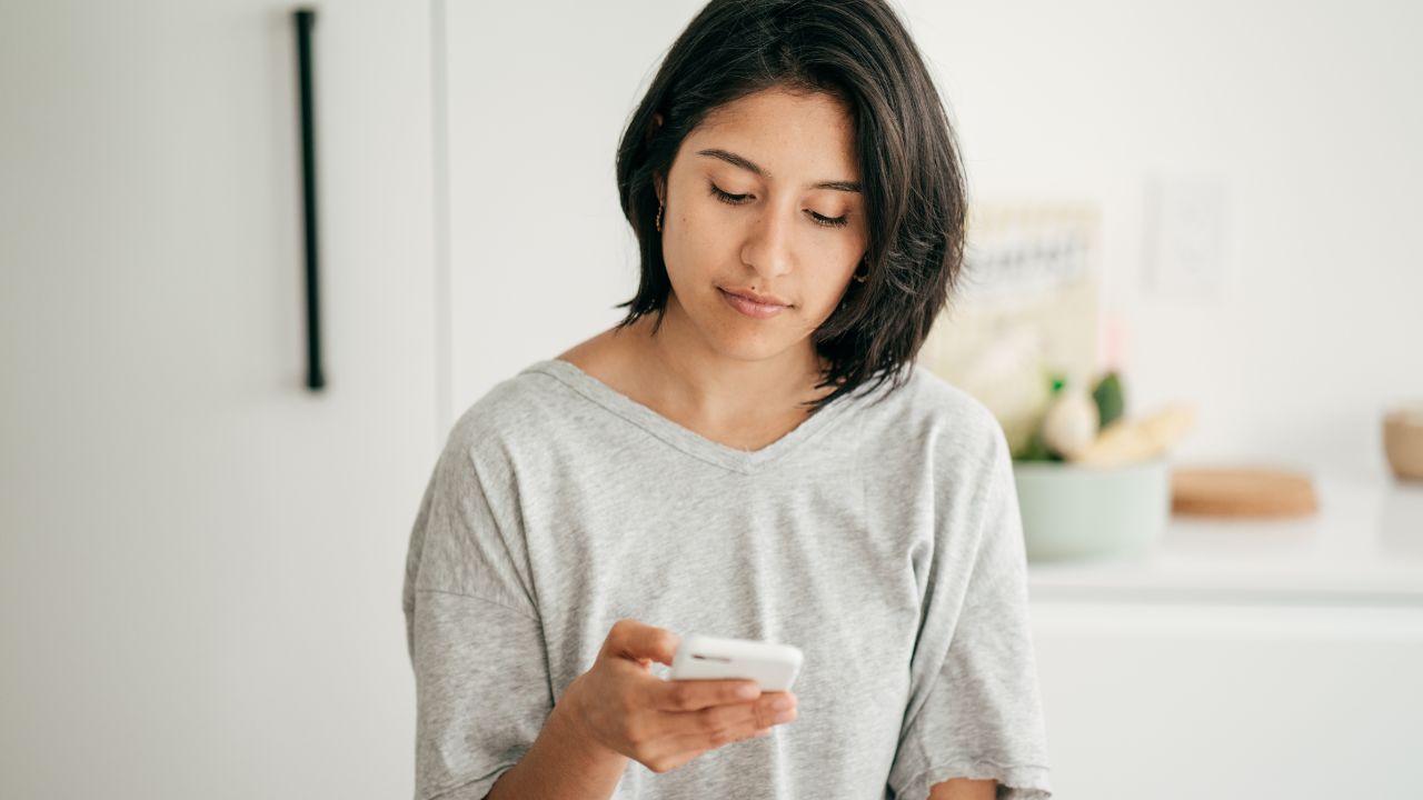 Junge Frau betrachtet lächelnd ihr Smartphone.