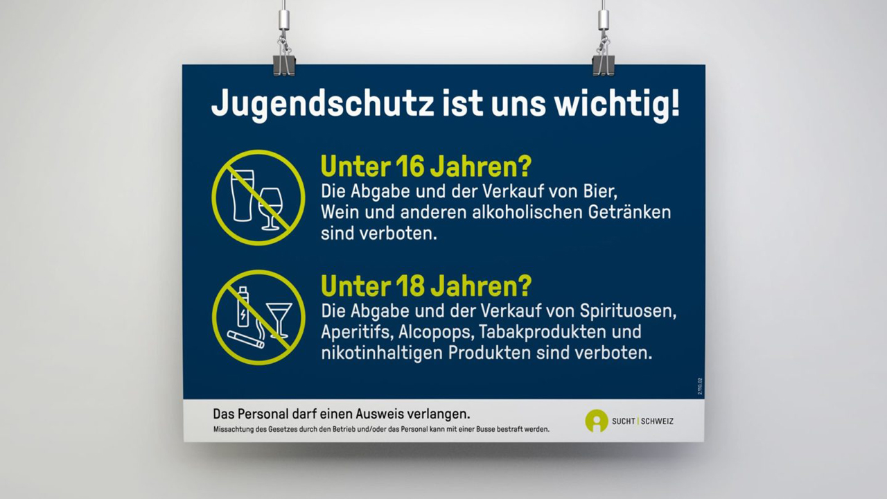 Ein blaues Schild hängt an zwei Ketten. Auf ihm steht: Jugendschutz ist uns wichtig! Unter 16 Jahren? Die Abgabe und der Verkauf von Bier, Wein und anderen alkoholischen Getränken sind verboten. Unter 18 Jahren? Die Abgabe und der Verkauf von Spirituosen, Aperitifs, Alcopops, Tabakprodukten und nikotinhaltigen Produkten sind verboten. Das Personal darf einen Ausweis verlangen. Missachtung des Gesetzes durch den Betrieb und/oder das Personal kann mit einer Buße bestraft werden. Sucht Schweiz.