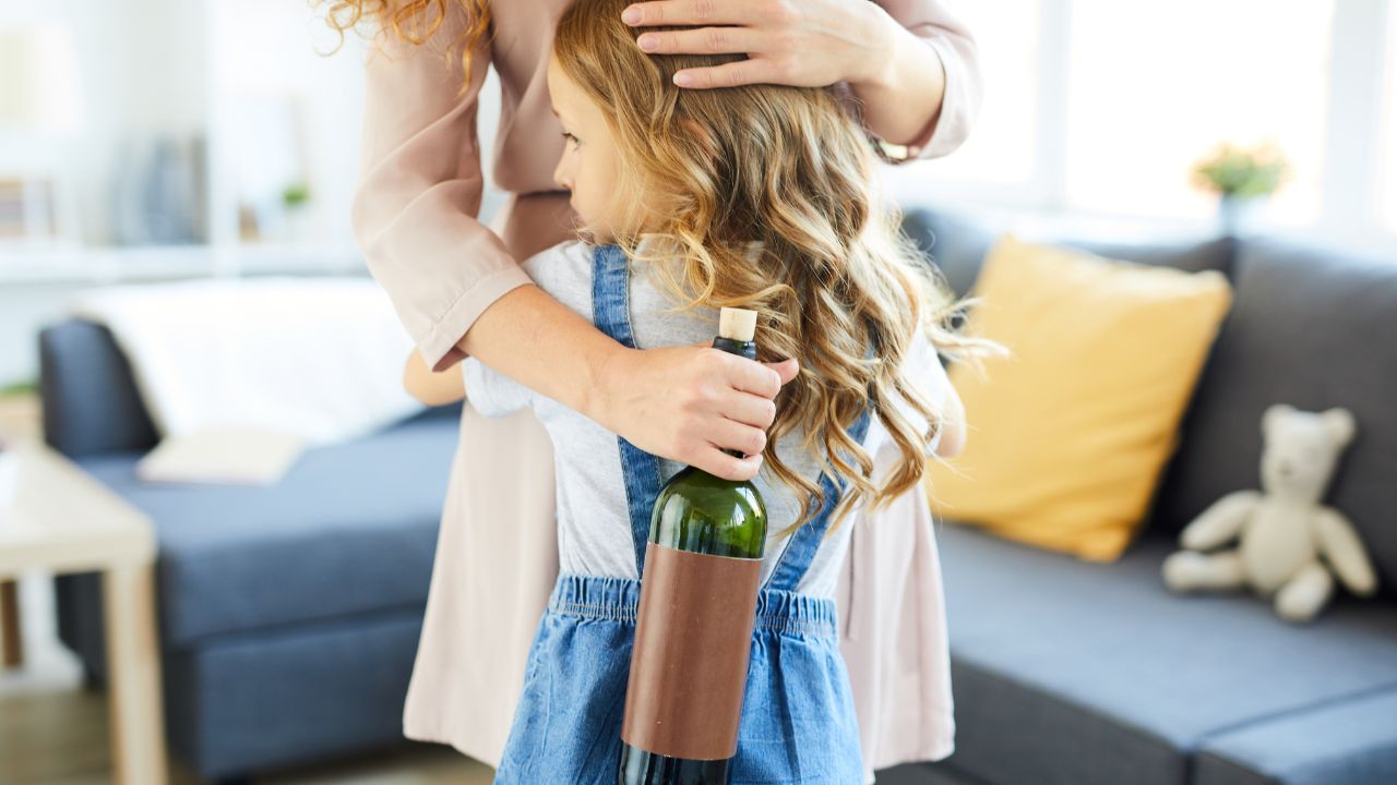 Mädchen umarmt seine Mutter, die eine Weinflasche in ihrer Hand hält.