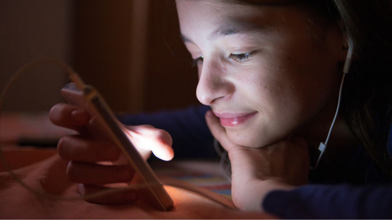 Jugendliches Mädchen mit Headset betrachtet ihr Smartphone im Dunkeln.