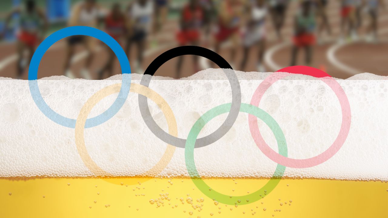 Die Olympischen Ringe versinken in Bierschaum. Im Hintergrund sind unscharf Läufer zu erkennen.