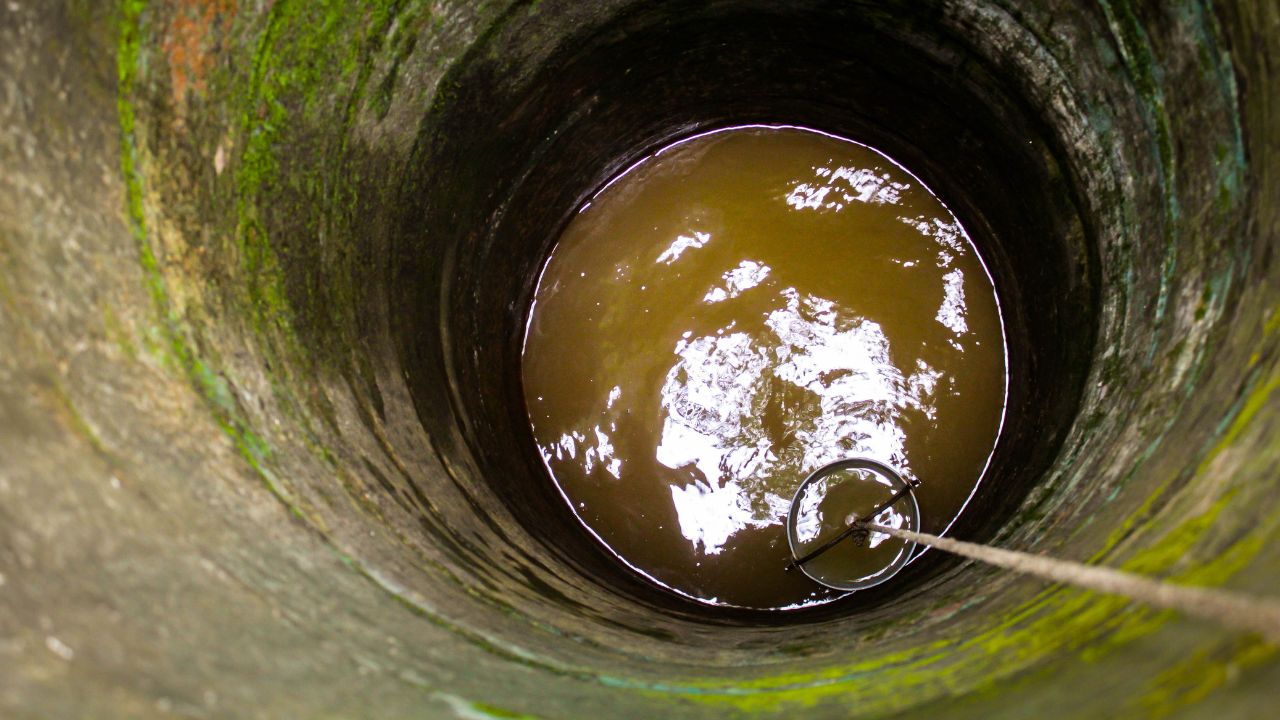 Ein Eimer wird an einem Seil in einen Brunnen abgesenkt.