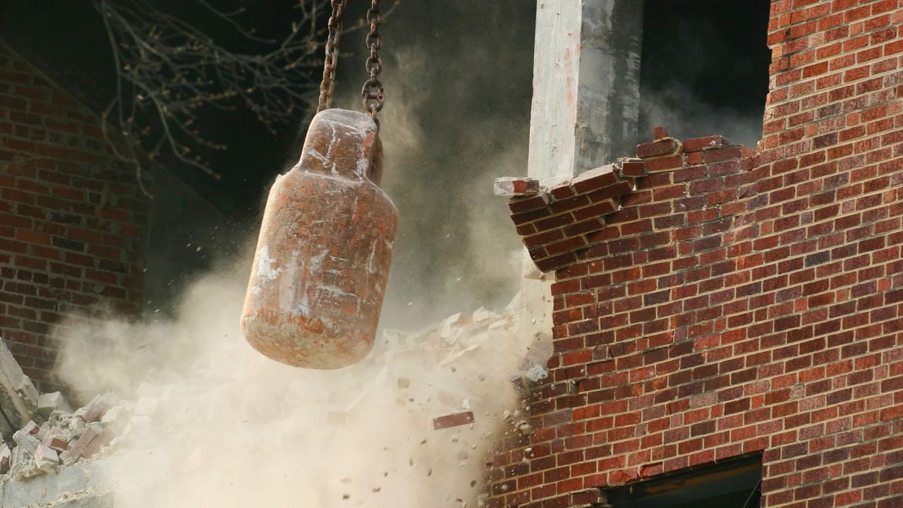 Abbruchbirne schlägt gegen eine Backsteinmauer, Staub und Trümmer fliegen.