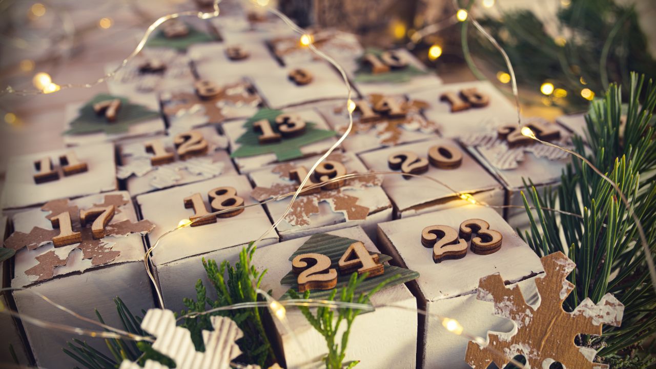 Selbstgemachter Adventskalender – Nahaufnahme kleiner Papierschachteln mit Holz-Zahlen, Papp-Schneeflocken, Lichterkette und Tannenzweigen.