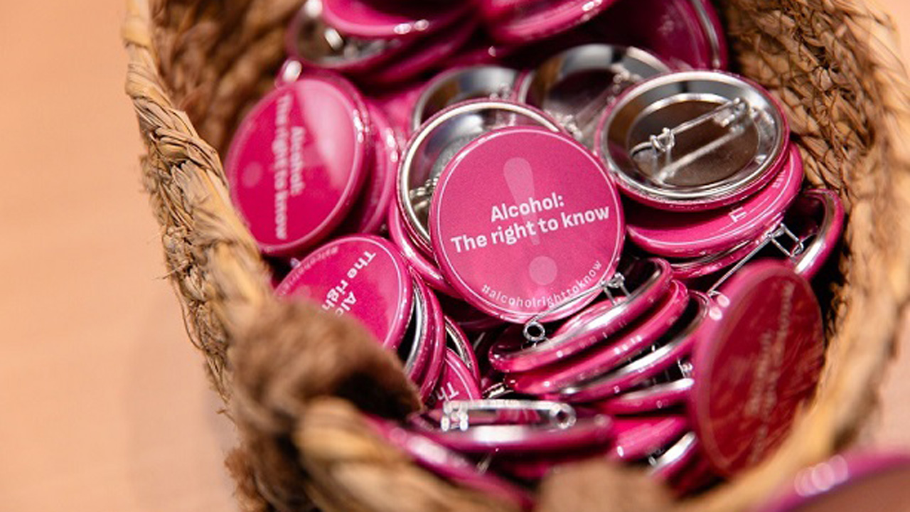 Eine Nahaufnahme eines geflochtenen Korbes voller pinker Ansteckbuttons mit der Aufschrift 'Alcohol: The right to know‘.