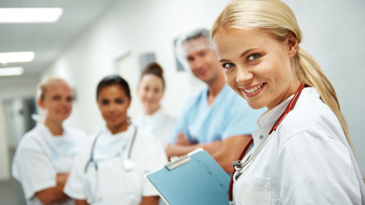 Eine Gruppe dynamischer junger Mediziner*innen steht im Flur eines Krankenhauses.