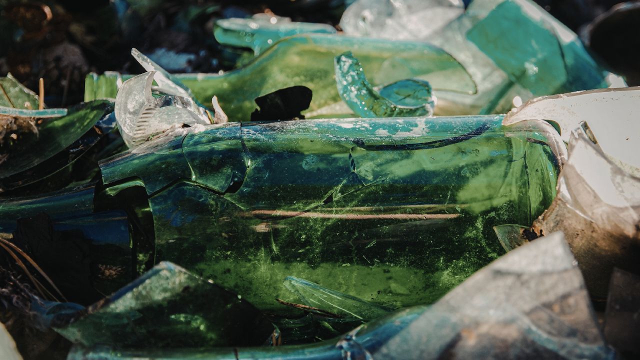 Eine Nahaufnahme eines Haufens grüner Glasflaschen, von denen einige zerbrochen sind, die ihre Strukturen und Farben zur Geltung bringen.
