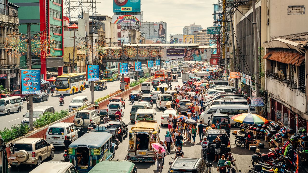 Chaotische und lebendige Straßenansicht in Manila mit unzähligen Fahrzeugen und Menschen, umgeben von Werbeanzeigen und Stromkabeln.