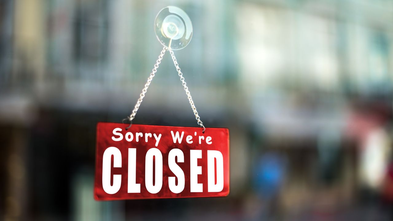 Rotes Schild mit weißer Schrift 'Sorry We're CLOSED' hängt mit Kette und Saugnapf an einem Glasfenster.