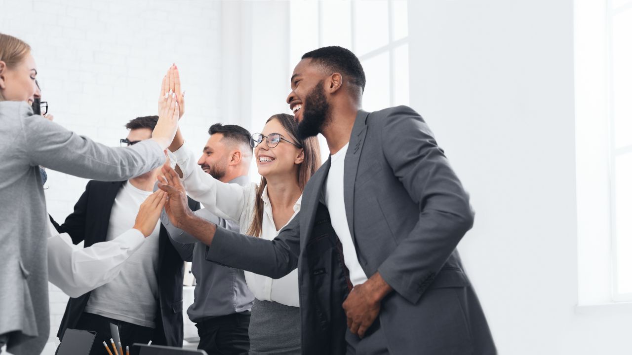Fünf junge Menschen in Geschäftsbekleidung beim High-Five.