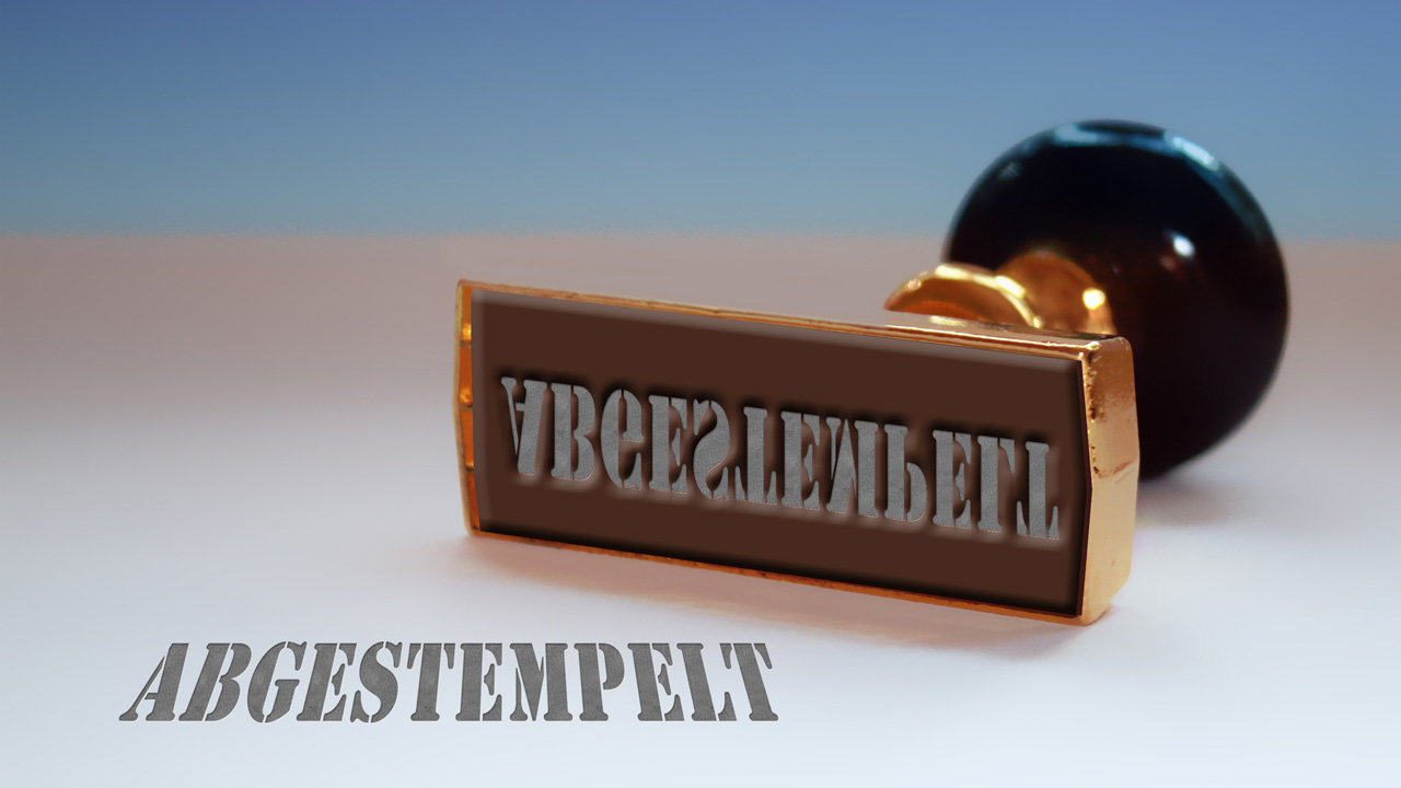 Ein edler Holzstempel mit Goldrand liegt auf der Seite und zeigt die Stempelplatte mit dem gespiegelten Wort ‚ABGESTEMPELT‘. Im Vordergrund steht das Wort lesbar in grauer Stencil-Schrift.