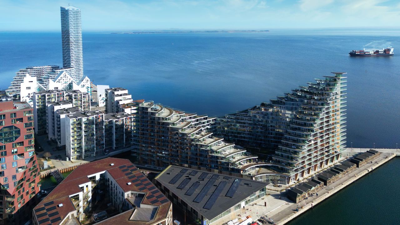 Luftaufnahme des modernen Stadtteils Aarhus Ø in Dänemark mit markanten terrassierten Wohngebäuden, dem Isbjerget-Komplex und dem Lighthouse-Hochhaus direkt an der blauen Ostsee.