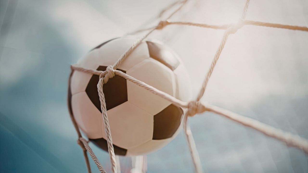 Schwarz-weißer Fußball, der ins Tornetz einschlägt – Nahaufnahme eines Treffers vor blauem Himmel.