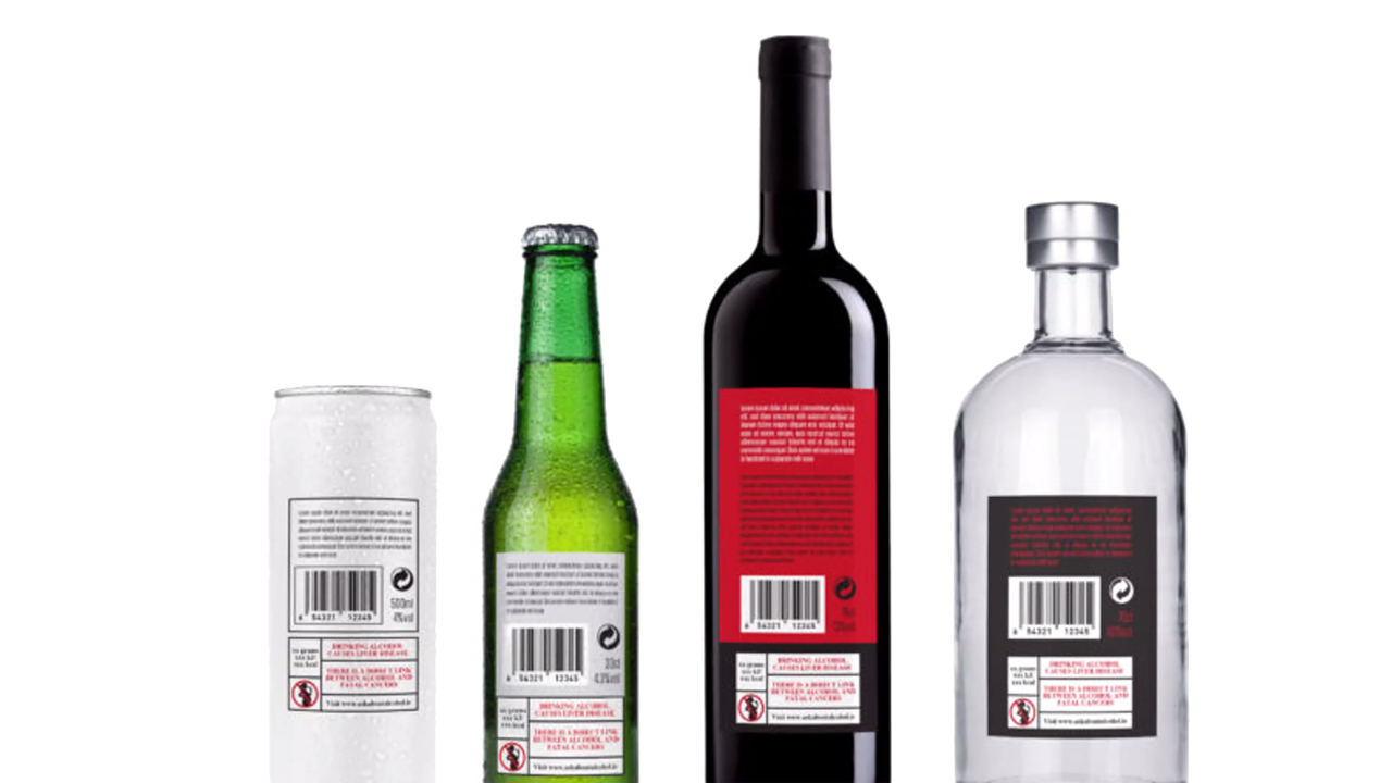 Vier Getränkeflaschen und -dosen von hinten auf weißem Hintergrund: eine silberne Dose, eine grüne Bierflasche, eine dunkle Weinflasche mit rotem Etikett und eine klare Schnapsflasche – alle mit Barcode und Warnhinweisen zum Alkoholkonsum.