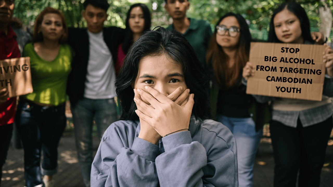 Junge kambodschanische Frau hält sich mit beiden Händen den Mund zu, im Hintergrund stehen mehrere junge Menschen mit Protestschildern, darunter eines mit der Aufschrift 'Stop Big Alcohol from Targeting Cambodian Youth'. Die Szene zeigt eine Protestaktion gegen Alkoholwerbung, die sich an kambodschanische Jugendliche richtet.