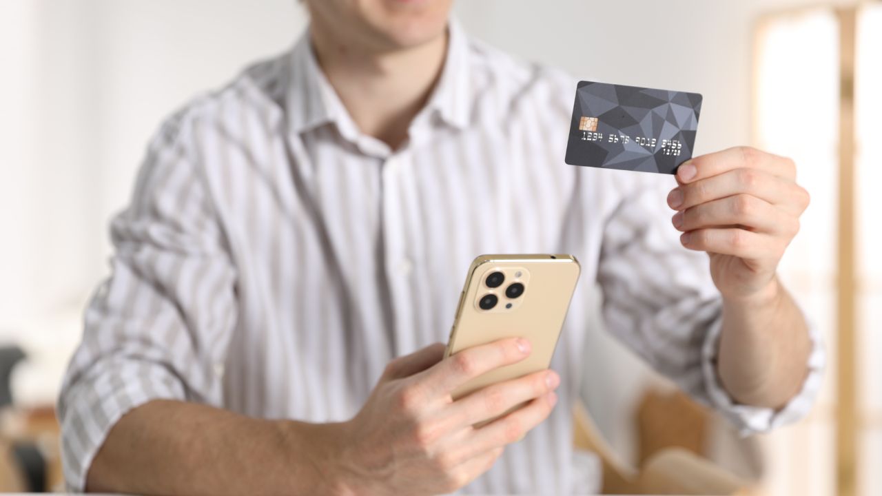 Person hält eine Kreditkarte in der einen und ein Smartphone in der anderen Hand.
