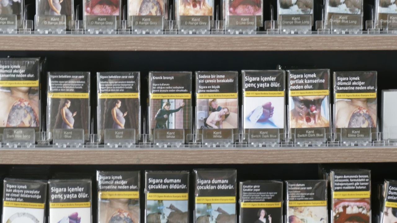 In Regalen stehen Reihen von Zigarettenpackungen mit anschaulichen Gesundheitswarnbildern, die auf türkisch auf die Gefahren des Rauchens hinweisen.