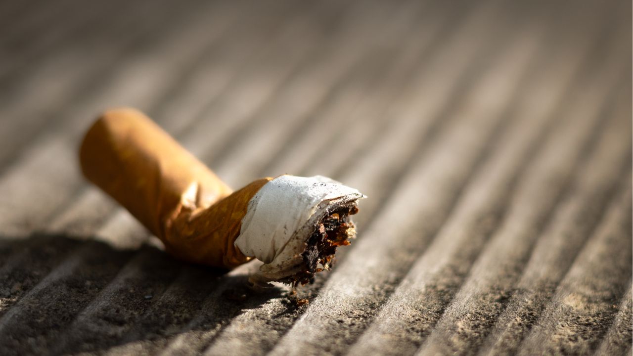 Makroaufnahme eines verbogenen gerauchten Zigarettenstummels mit Restasche, liegend auf gerillter Betonoberfläche, geringe Schärfentiefe.