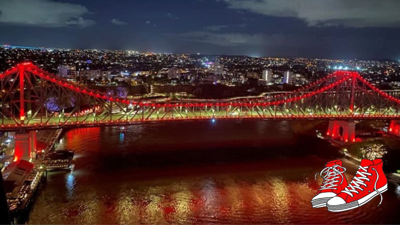 Luftaufnahme der Story Bridge in Brisbane, die am 9. September anlässlich des FASD-Tages in rotes Licht getaucht wird. Rechts unten sind zwei rote Turnschuhe als Erkennungszeichen der internationalen Kampagne Red Shoes Rock zu sehen.