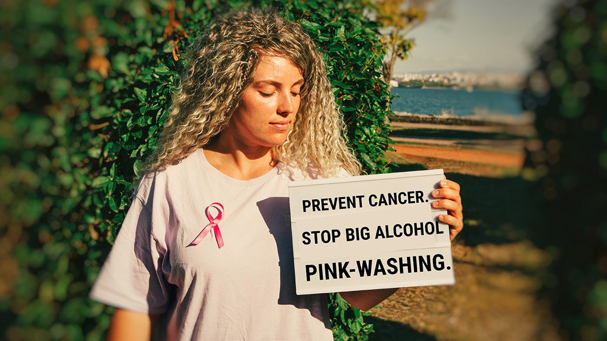 Frau mit Schild, auf dem 'Prevent Cancer. Stop Big Alcohol pink-washing' steht