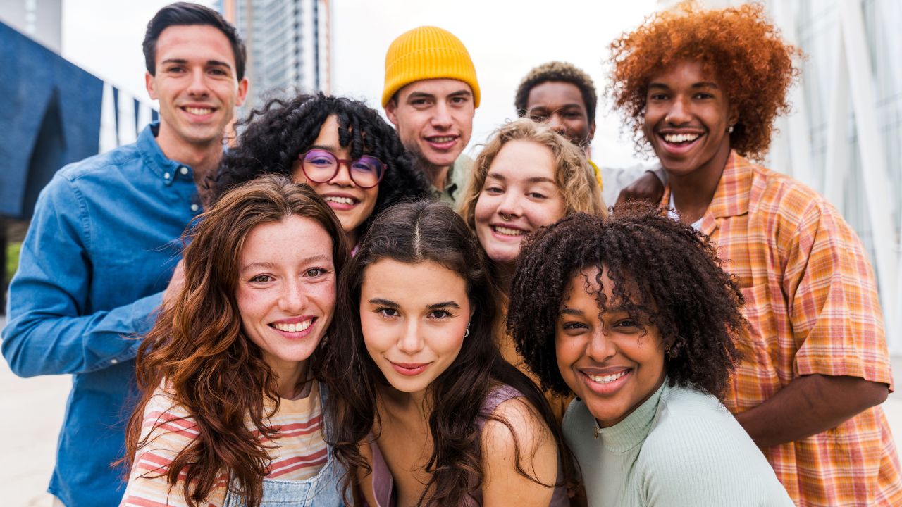 Eine fröhliche, ausgelassene, multikulturelle Gruppe junger Freund*innen, die gemeinsam Zeit im Freien verbringt.