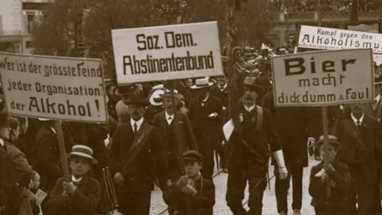 Foto eines Demonstrationszuges zu Beginn des 20. Jahrhunderts. Verschiedene darin getragene Transparente weisen auf den Sozialdemokratischen Abstinentenbund hin: 'Wer ist der größte Freind jeder Organisation? Der Alkohol!', 'Kampf gegen den Alkoholismus' sowie 'Bier macht dick, dumm und faul'.