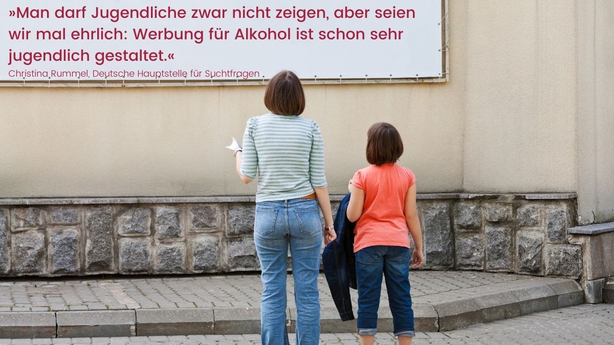 Mutter und Tochter stehen vor einer weißen Werbetafel. Darin das Zitat von DHS-Geschäftsführerin Christina Rummel: Man darf Jugendliche zwar nicht zeigen, aber seien wir mal ehrlich: Werbung für Alkohol ist schon sehr jugendlich gestaltet.