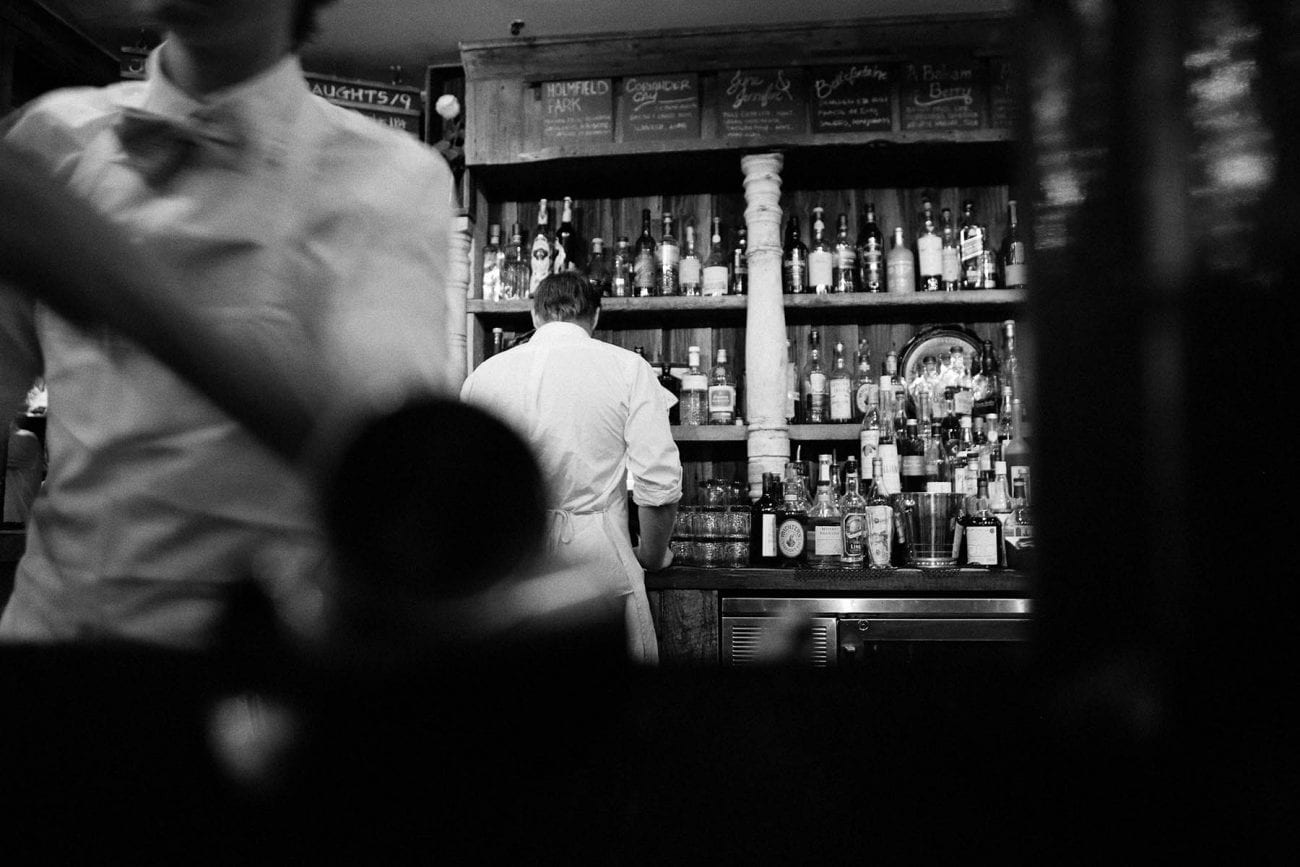 Schwarz-Weiß-Foto einer Bar mit Rückenansicht eines Barkeepers.